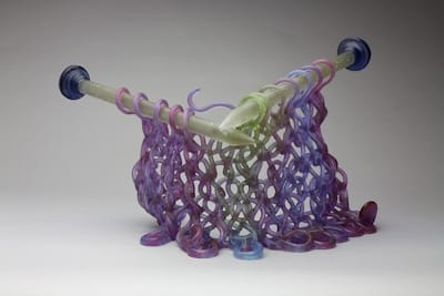 Canadian-American glass artist Carol Milne creates “knitted glass” sculptures, like <i>Purple Reigns</i> (c. 2016), thus combining the traditionally “feminine” craft of knitting with the traditionally “masculine” art of glass working. To arrive at these forms, she knits wax strands and then uses the lost wax casting method to cast the form in glass.